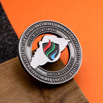 Antique silver challenge coin for SoCo Emergency featuring a colorful shield logo over a map cutout and raised text on the outer rim.