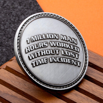 Antiqued silver challenge coin featuring 1 Million Man Hours Worked Without Lost Time Incident text on a wooden surface.