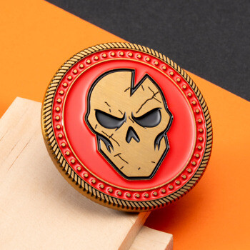 Challenge coin featuring a cracked bronze skull on a red enamel background with a rope border and studded detailing.