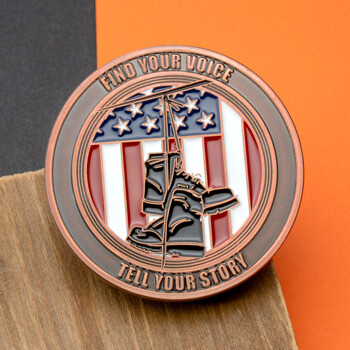Antique copper challenge coin featuring combat boots hanging over a wire against an American flag background with the text Find Your Voice Tell Your Story.