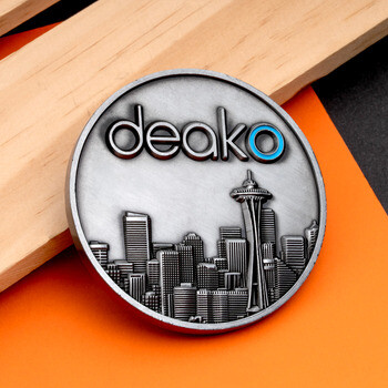 Antique silver challenge coin featuring the Deako logo and an embossed Seattle skyline with the Space Needle.