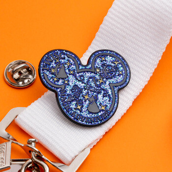 Mickey Mouse silhouette lapel pin with blue glitter enamel and starry theme, attached to a white lanyard on an orange background.