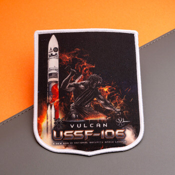 Printed embroidered patch depicting the Vulcan USSF-106 rocket launch with a blacksmith figure surrounded by fire and embers