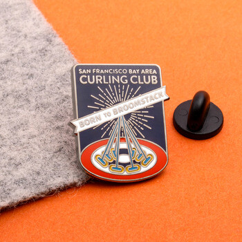 San Francisco Bay Area Curling Club enamel lapel pin with black rubber clutch next to it on an orange and gray background